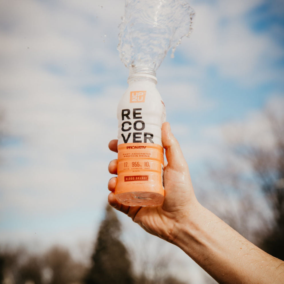 Hand holding bottle up to the sky with clear liquid spilling out.