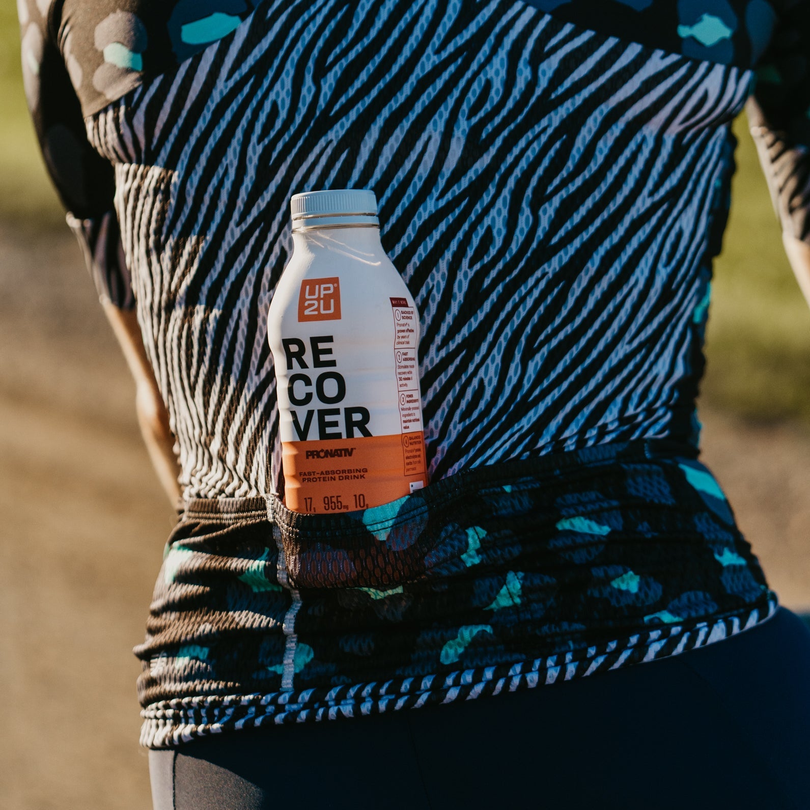 Bottle of UP2U recovery drink tucked into back pocket of cyclist's jersey.